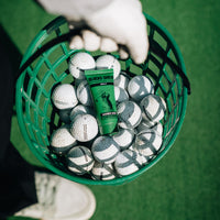 Green Gamer Grip for Golf tube resting in a basket of driving-range balls, held by a gloved hand