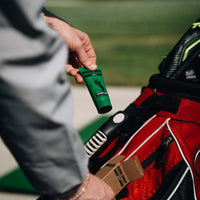Golfer taking a green Gamer Grip for Golf tube from a red golf bag on the course, with the kraft box in the bag pocket